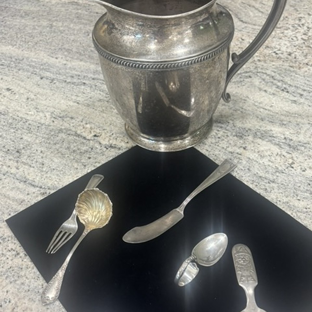 A sterling silver water pitcher with sterling flatware — fork, shell serving spoon, butter knife and souvenir spoons